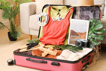 Open suitcase with beach accessories and palm leaves in living room