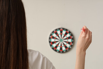 Young woman playing darts on light background