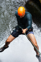 Latin american man practicing canyoneering sport, descending a waterfall with ropes and safety...