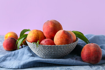 Bowl of fresh peaches on table against lilac background