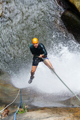 Latin american man enjoys canyoneering, rappelling down waterfall, experiencing extreme sport and...