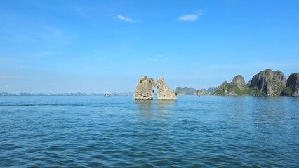 A scenic view of the iconic Kissing Rocks rising from the calm emerald waters of Ha Long Bay,...