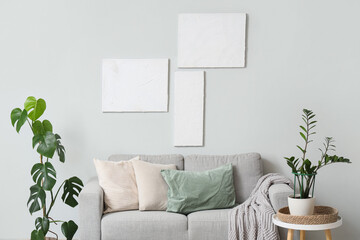 Interior of stylish modern living room with grey sofa, houseplants and pictures
