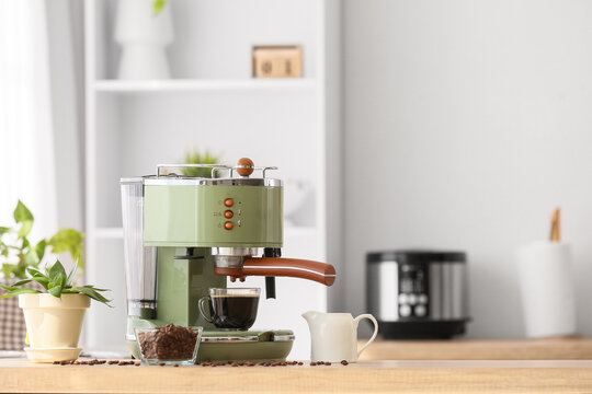 Modern coffee machine with cup and beans on table in kitchen