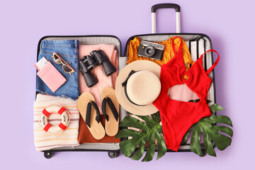 Open suitcase with clothes, swimsuit, beach accessories and binoculars on lilac background, closeup