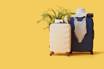 Suitcases, swimsuit and beach accessories on yellow background, closeup