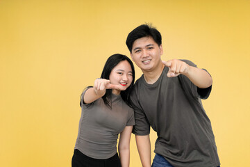Fototapeta premium playful couple asian pointing at you in studio yellow background