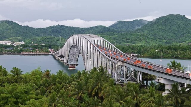 Drone orbit of San Juanico Bridge with palm trees in front and mountains in the background.
