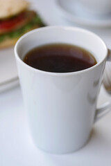 Hot beverage in white cup on table with sandwich nearby