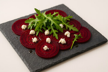 Beetroot carpaccio on a slate tile with goat cheese and arugula