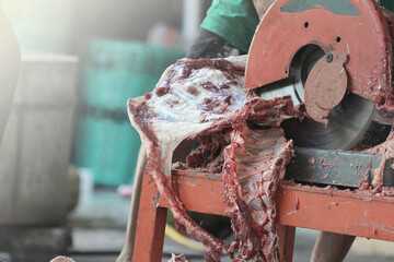 close up of a man cutting beef ribs using a grinder cutting machine