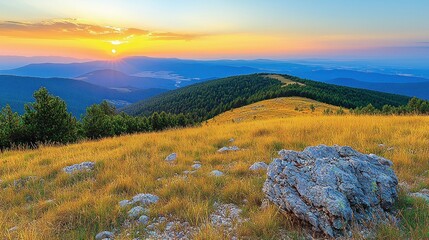 Mountaintop vista at sunset.  Golden, dry grass covers a mountain ridge, a large rock sits centrally.  Distant, layered mountain ranges are visible beneath a colorful sunset sky