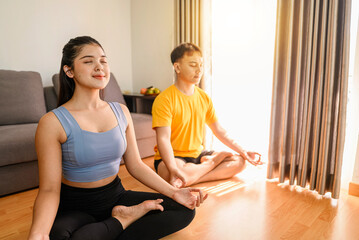 Indonesian southeast asian couple meditating in the lotus position on yoga at home for a healthy lifestyle and body care. Meditation and yoga practices concept