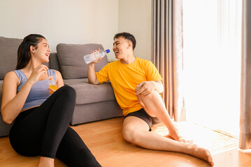 Indonesian southeast asian couple drinking water after finishing a home body workout exercise session for a fit physique and a healthy sport lifestyle at home. Fitness and active lifestyles concept