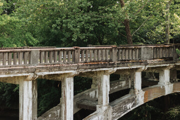 Weathered concrete bridge balustrade and railing spanning lush forest landscape with moss-stained...