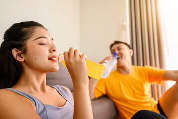 Indonesian southeast asian couple drinking water after finishing a home body workout exercise session for a fit physique and a healthy sport lifestyle at home. Fitness and active lifestyles concept