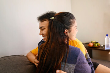 Indonesian southeast asian affectionate couple embracing while sitting on the couch at home
