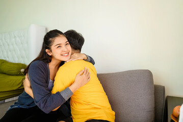 Indonesian southeast asian affectionate couple embracing while sitting on the couch at home