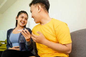 Indonesian southeast asian couple sitting on a sofa at home while looking results of a pregnancy test. Healthcare and family planning concept