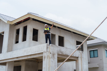 A man is standing on a roof of a building. He is wearing a yellow vest. The building is in the process of being renovated