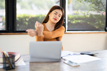 A young woman stretches at her desk in a home office, taking a relaxing break from work. The bright...