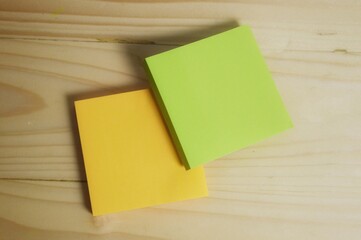 Two sticky notes, one yellow and one green, placed on a wooden surface, creating a simple and...