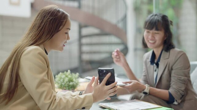 Two women are sitting at a table with a cell phone in front of them. One of the women is holding the phone