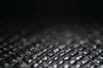 A high-definition macro shot of a textured, dark surface with intricate patterns and glossy...