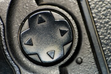 A macro shot of a black directional control button, showcasing the detailed texture of the surface and arrows for navigation