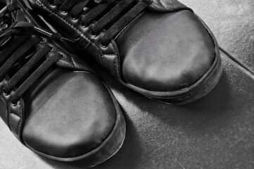A black-and-white close-up of a pair of black leather shoes with laces, highlighting their glossy and rugged texture