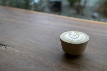 A cup of latte art on a wooden table facing the window in cafe