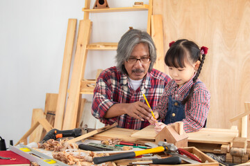 Asia retirement carpenter man spends time with cheerful granddaughter in carpentry studio, aged...