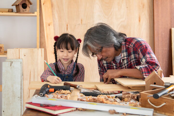 Asia retirement carpenter man spends time with cheerful granddaughter in carpentry studio, aged...