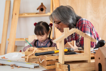 Asia retirement carpenter man spends time with cheerful granddaughter in carpentry studio, aged...