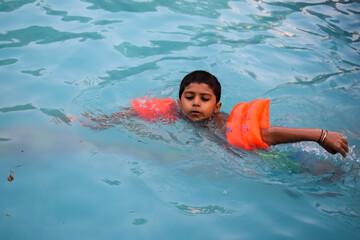 Happy Indian boy swimming in a pool, Kid wearing swimming costume along with air tube during hot...