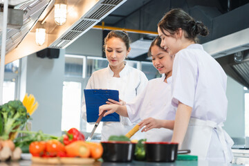 Culinary Instructor Guides Students in a Professional Kitchen, Women in Chef Uniforms Preparing Food in a Commercial Kitchen, Young Chefs Learning to Cook with Fresh Ingredients