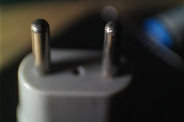 Close-up of a two-pronged electrical plug in soft focus, highlighting the metal pins and plastic...