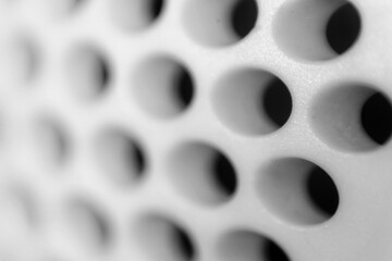 Obraz premium Close-up of a perforated surface with evenly spaced circular holes, captured in black and white