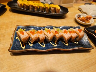 Sushi rolls with grilled topping lined up on ceramic plate, ideal for restaurant ads, Asian food...