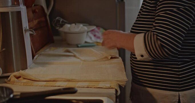 Senior woman layering phyllo dough in her home kitchen. She is preparing a delicious meal.