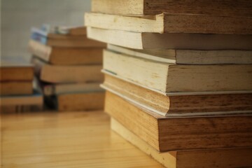 Close-up of a stack of old, worn books on a wooden table, with blurred books in the background,...