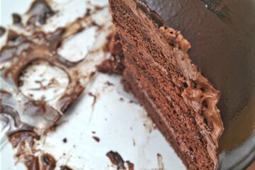 Close-up of a slice of rich, decadent chocolate cake with creamy frosting, displayed on a white...