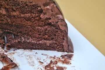 Close-up of a slice of rich, decadent chocolate cake with creamy frosting, displayed on a white...