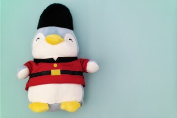 A cute penguin plush toy dressed as a royal guard, standing against a simple teal background