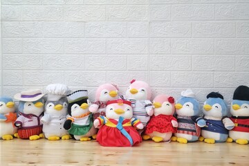 A lineup of penguin plush toys, each dressed in unique and colorful costumes, arranged on a wooden surface against a white textured wall. Perfect for playful, creative, and children's themes.