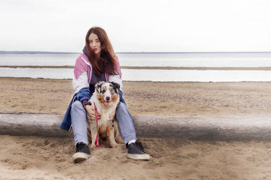 Caucasian brunete woman sit with blue merle Australian shepherd dog on a beach copy space