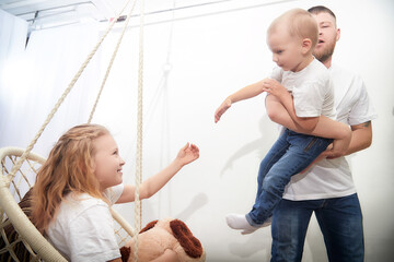 Child plays joyfully with parent while sibling engages in fun activity indoors on a bright day