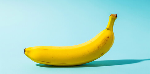 Single yellow banana on a light blue background with shadow.