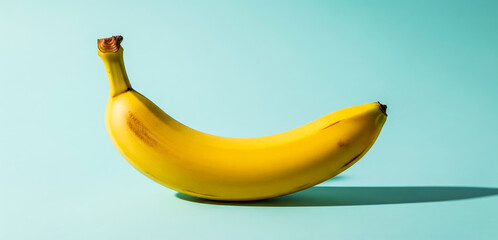Single yellow banana fruit on a light blue background with shadow.