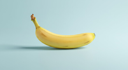 A single yellow banana lies on a light blue surface with soft lighting.